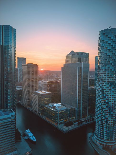 An expansive aerial view of a modern city skyline under a partly cloudy sky with a mix of tall glass skyscrapers and mid-rise office buildings. The foreground features a variety of residential apartme